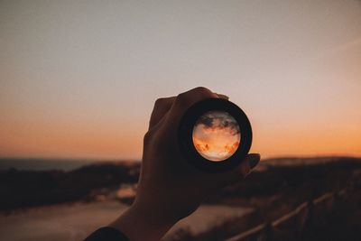 Close-up of woman hand holding lens against clear sky during sunset