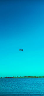 Airplane flying over sea against clear blue sky