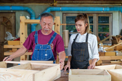 Tutor with female carpentry student in workshop studying for apprenticeship at college ,