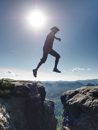 Man jumping on rock formation against sky