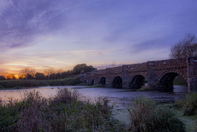 Arch bridge over river against sky during sunset