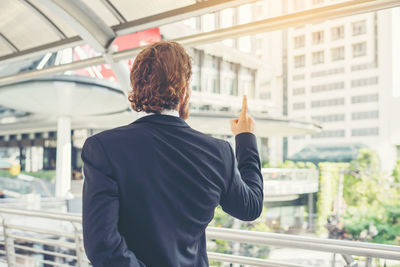 Rear view of young businessman gesturing while standing on elevated walkway 