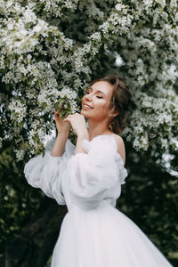 Beautiful bride in a wedding dress walks in a blooming apple-tree park in spring