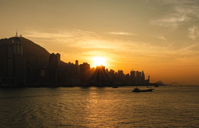 Silhouette buildings by sea against sky during sunset