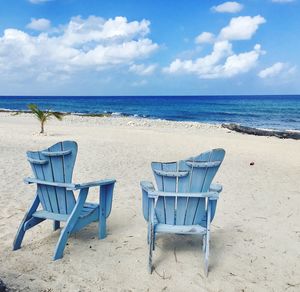 Deck chairs on beach against sky