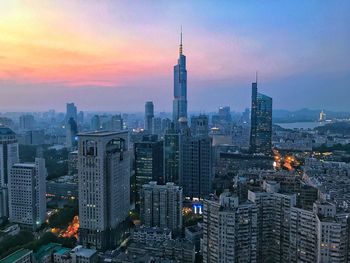 Illuminated buildings in city against sky during sunset