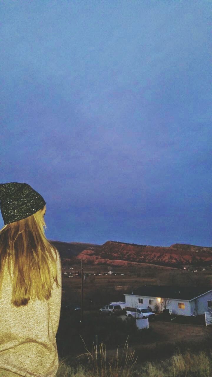 REAR VIEW OF WOMAN BY HOUSE AGAINST SKY