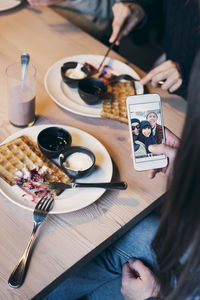 Cropped image of woman looking at photograph on smart phone screen while having breakfast with friends