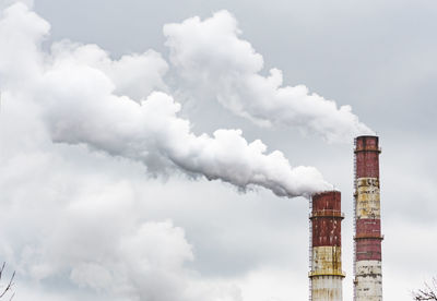 Thick white smoke from industrial factory old rusty chimneys on a cloudy grey sky background