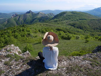 Rear view of woman in large floppy hat in lush mountains