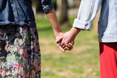 Midsection of lesbian couple holding hands on field