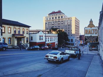 Cars on street by buildings against sky in city