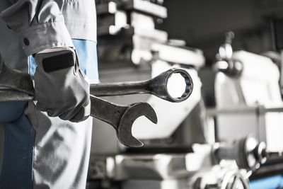 Midsection of worker holding equipment while standing in factory