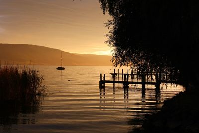 Silhouette wooden posts in lake against sky at sunset