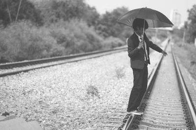 Businessman with umbrella standing on railroad track