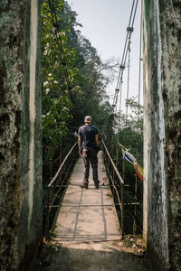 Rear view of man standing on rope bridge against trees