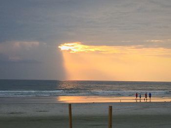 Silhouette people standing on beach against sky during sunset