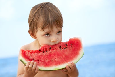 Portrait of boy eating apple against sky