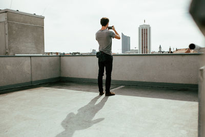 Rear view of man photographing on building terrace during sunny day