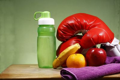 Close-up of fruits with boxing gloves and water bottle on table against green background