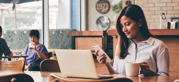 Young woman using mobile phone while sitting on table