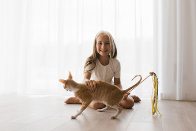 Caucasian teenage girl plays with a cornish rex cat at home on a sunny day