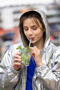 Beautiful attractive young woman or twentysomething girl drinking cold mojito in city center