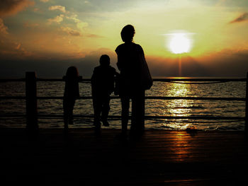 Silhouette people standing at beach during sunset