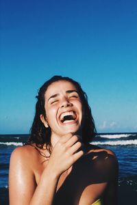 Happy young woman at beach against clear blue sky