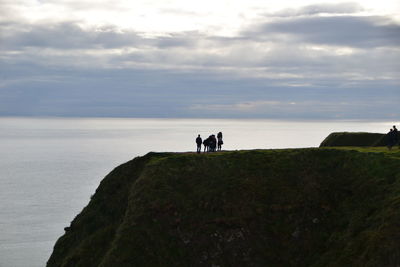 Silhouette people on rock by sea against sky