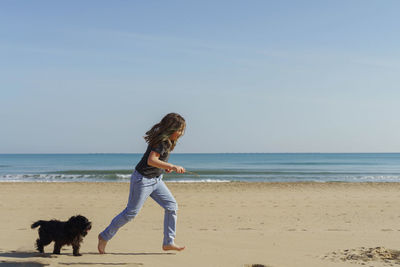 Rear view of girl running at beach against sky