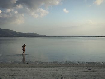 Rear view of sensuous woman walking in sea against sky