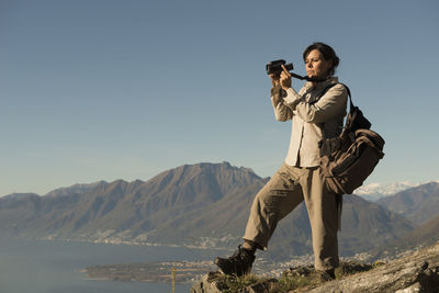 Female hiker photographing on cliff against swiss alps