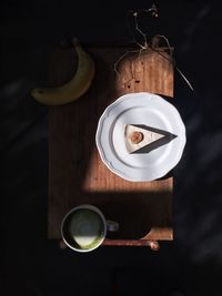 Directly above view of fresh cake slice served with banana and matcha tea on table