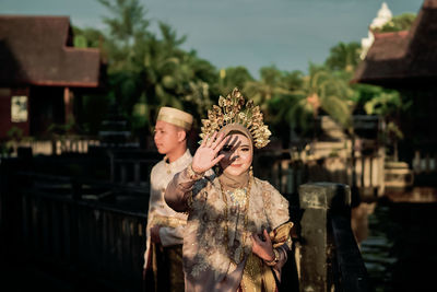 Portrait of bride wearing traditional clothing shielding eyes while standing with groom