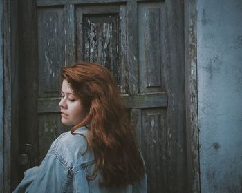 Rear view of young woman standing by old closed door