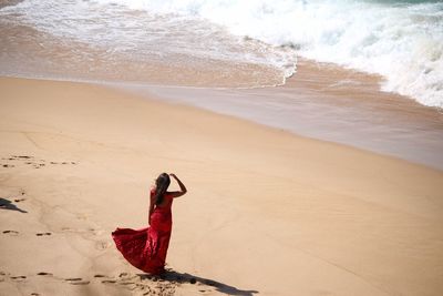 Full length of woman in red dress standing on beach against sky