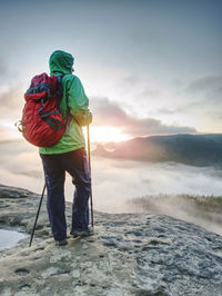 Tourist in green windcheater with hood on head and red backpack on back enjoy amazing  wild nature.