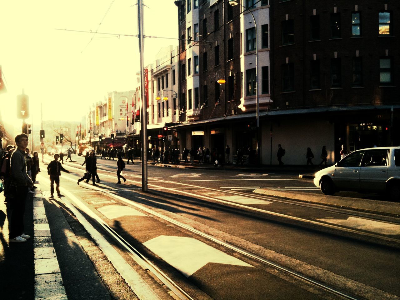 transportation, building exterior, architecture, city, built structure, street, mode of transport, city life, car, land vehicle, walking, city street, public transportation, railroad track, men, on the move, person, road, incidental people