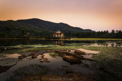 Scenic view of lake by buildings against sky during sunset