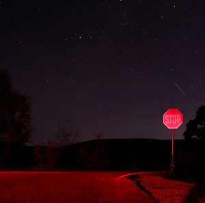 Road sign on field against sky at night