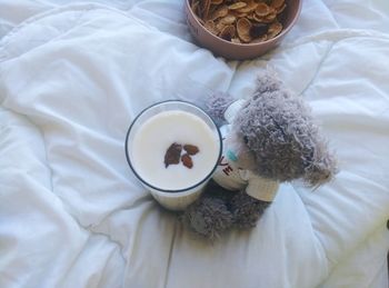 High angle view of teddy bear with milk glass and breakfast cereal on bed