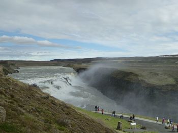 People by waterfall against sky