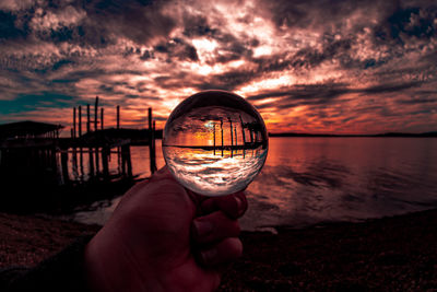 Reflection of person hand on glass against sea during sunset