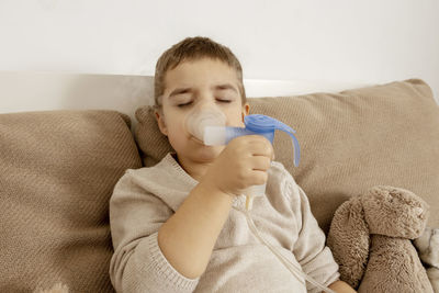 Sick little boy with inhaler for cough treatment. unwell kid doing inhalation on his bed. flu season