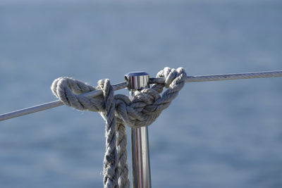 Close-up of rope tied on metal rod against sea