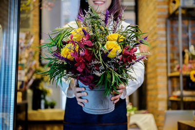 Midsection of smiling woman holding flowers at home