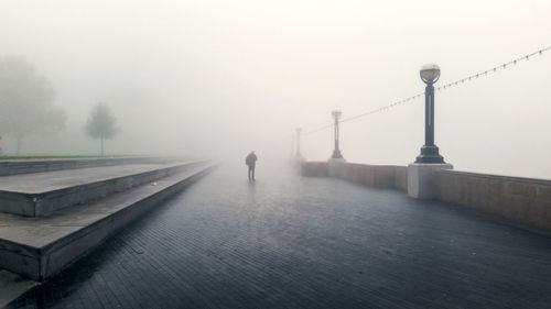 Rear view of silhouette man standing pedestrian zone against sky during foggy weather