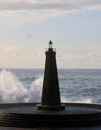 Lighthouse against sky, waves crashing in from sea