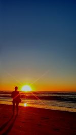 Silhouette man standing on beach against sky during sunset